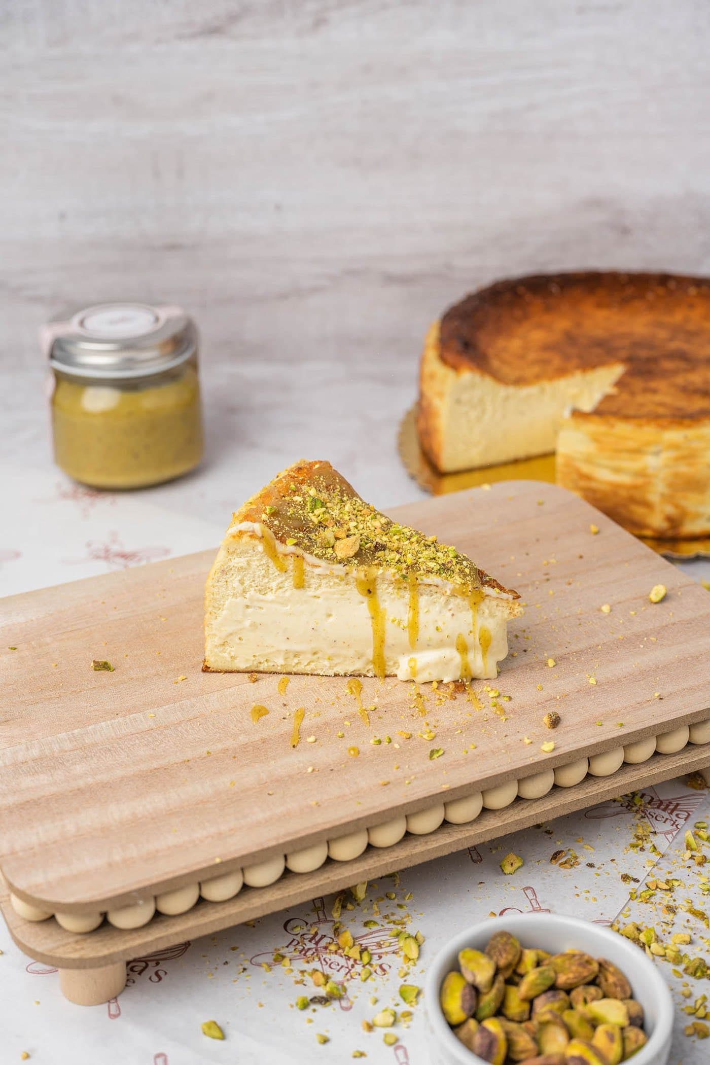 Pistachio Basque cheesecake slice served on a wooden board with crushed pistachios and honey drizzle